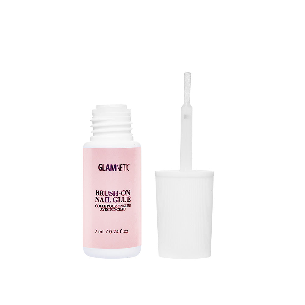 A small glamnetic Brush-On Nail Glue bottle with a pink label sits by its white cap. The upright brush applicator, coated in glue, is ready for salon-style nails or applying glamnetic Press On Nails.