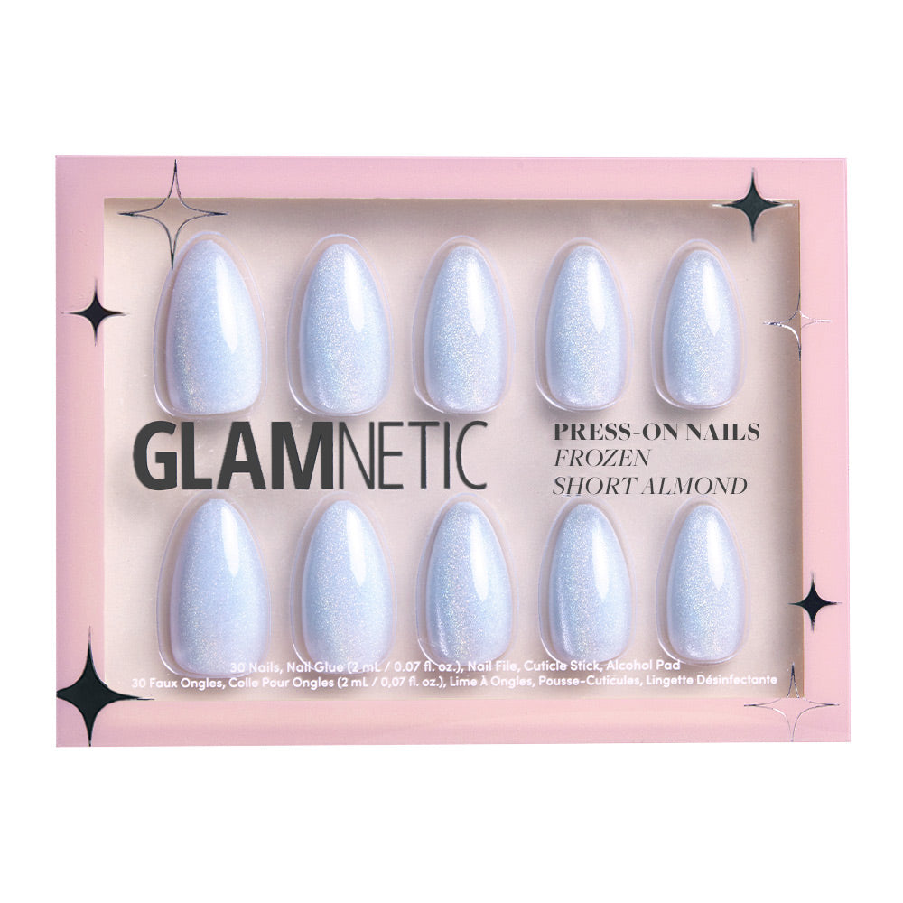 A box of glamnetic Frozen press-on nails features ten short almond-shaped, sparkly iridescent white nails with an icy-blue tint, arranged in two rows against a pink background.