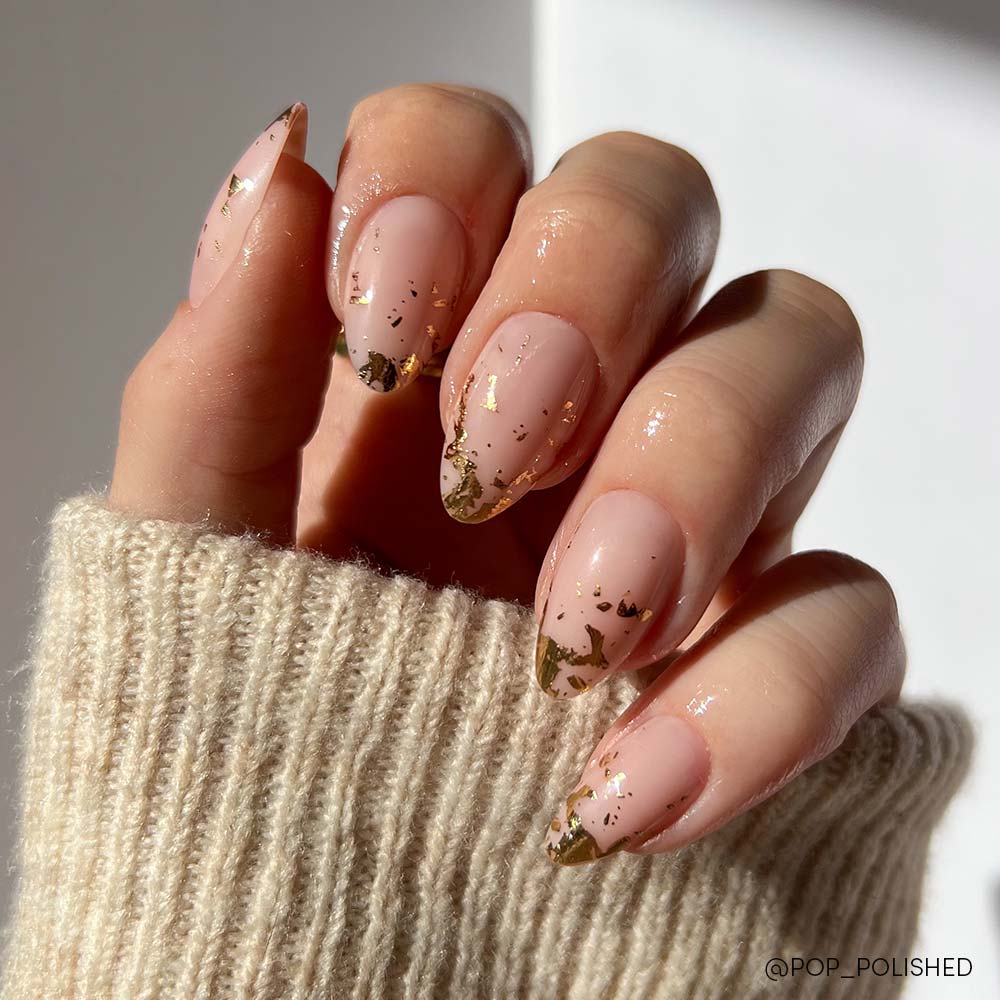 The glamnetic 24K short almond press-on nails showcase a nude pink base with gold foil details, complemented by a cream knitted sweater sleeve.