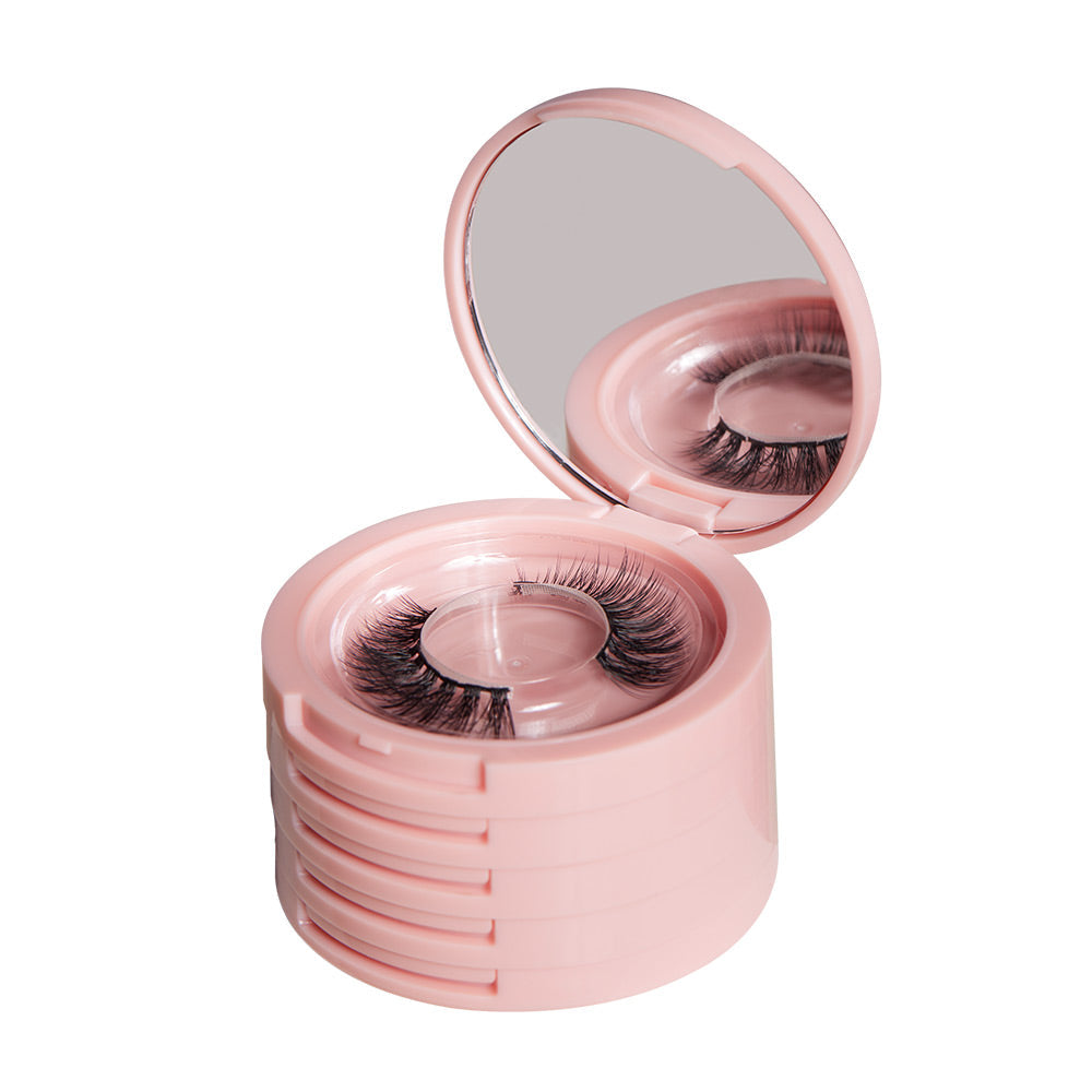 The glamnetic Glam & Go Travel Case is a pink circular container with a built-in mirror, holding several pairs of Glamnetic Lash Extensions in separate compartments. The open case displays one set of magnetic lashes and the mirror.