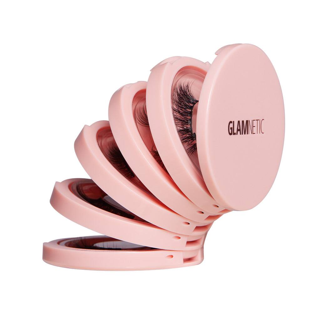 Four pink, round Glam & Go Travel Cases by glamnetic are fanned out, each holding a pair of magnetic lashes. The outer case features the glamnetic logo—ideal for storing your lash extensions on the go.