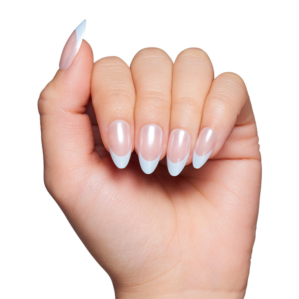 A hand with light skin tone displays manicured, almond-shaped nails in glamnetics Blueberry Icing: a pale pink base with a glazed finish and baby blue French tips. The background is white.