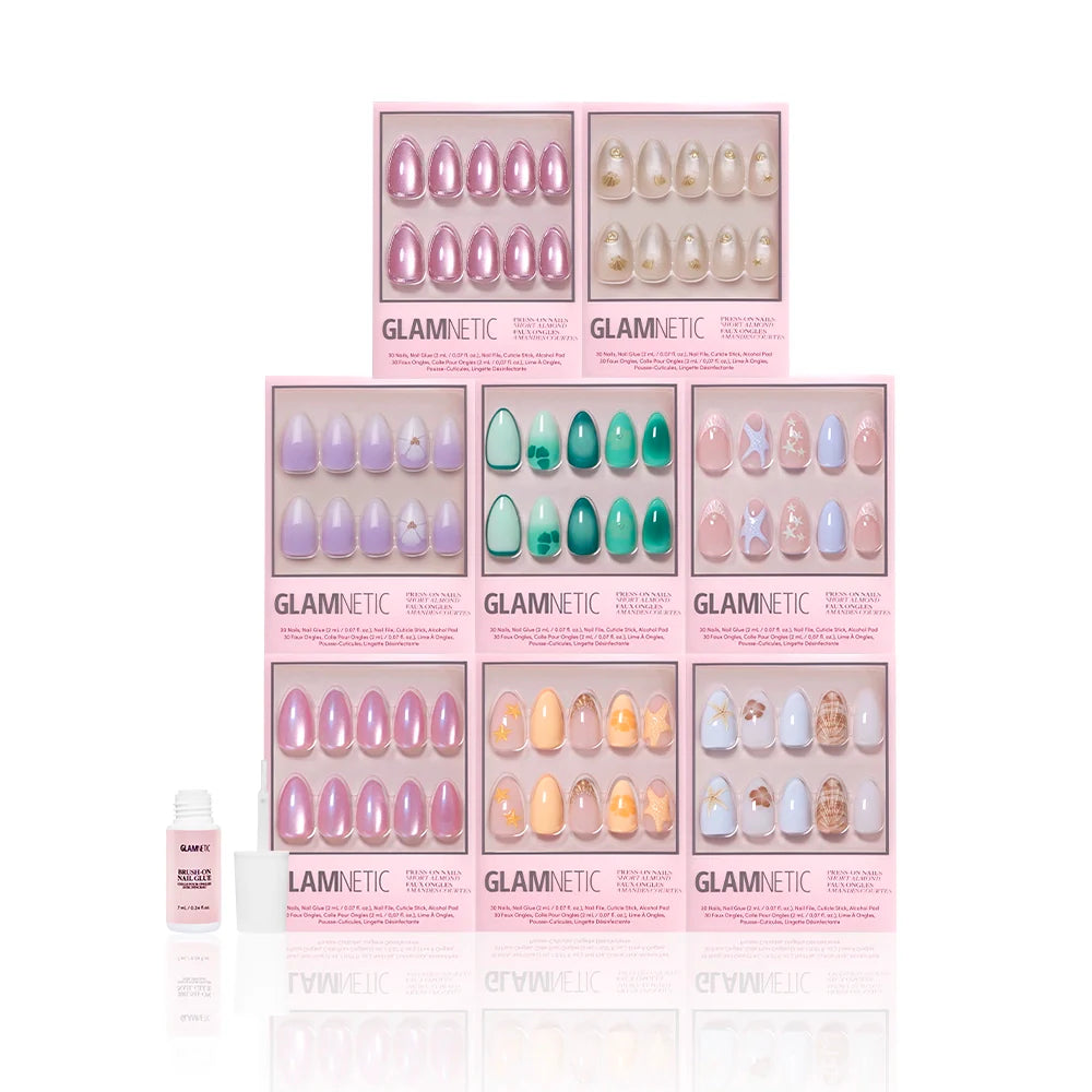 Eight Glamnetic press-on nail boxes, including the Almonds At Sea set, are stacked in a pyramid. A small nail glue bottle is on the left. The scene has a white background.