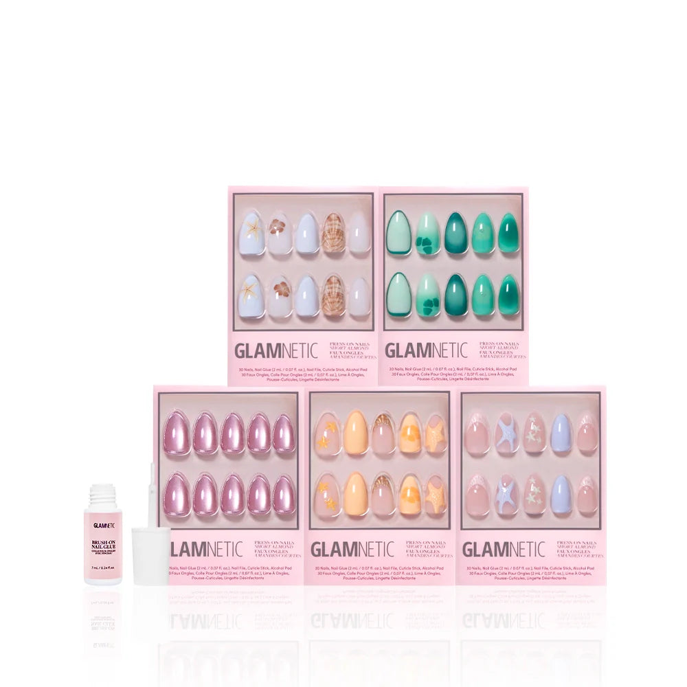 Five boxes of glamnetic Ann’s Cove press-on nails with assorted colors and designs—featuring coastal scenes and 3D art—are arranged in two rows beside a small nail glue bottle, all set against a white background.
