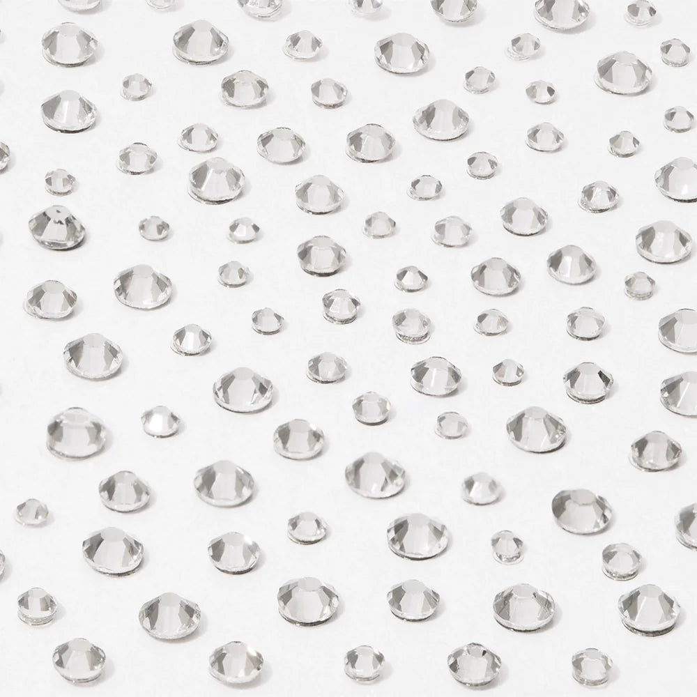 Multiple clear, round, faceted gems of different sizes are scattered on a white surface, creating a sparkling effect—perfect to use with glamnetic’s A Gem Nail Decal Stickers for stunning nail art designs.