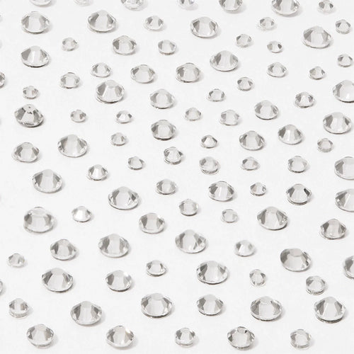Multiple clear, round, faceted gems of different sizes are scattered on a white surface, creating a sparkling effect—perfect to use with glamnetic’s A Gem Nail Decal Stickers for stunning nail art designs.