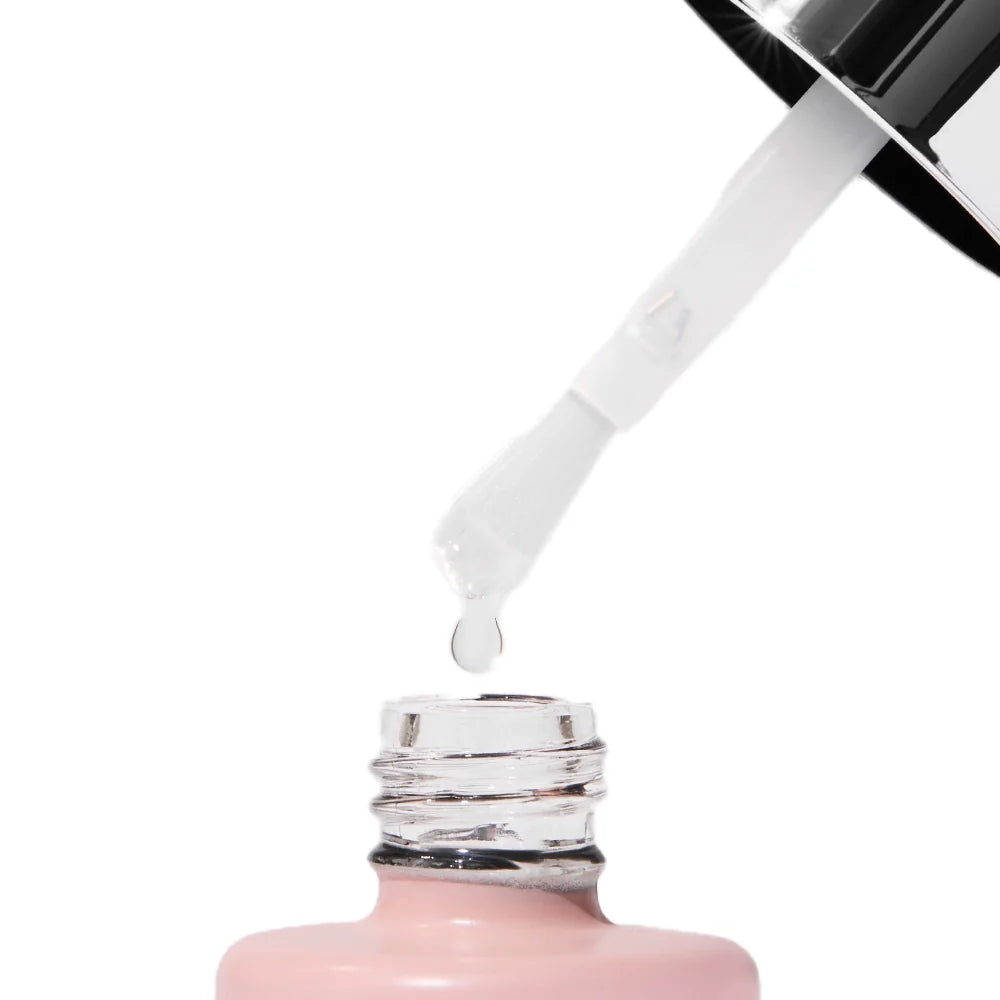 A close-up of a nail polish brush with a clear drop about to fall into an open light pink bottle, ideal for a salon-quality look when you pair it with the glamnetic UV Gel Clear Top Coat.