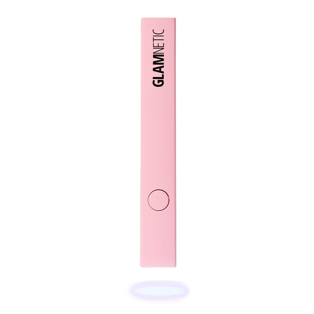 The glamnetic Handheld UV LED Lamp is a slim, rectangular, light pink device with a circular center button and GLAMNETIC printed vertically in black—perfect for gel or press-on nails. Shown on a white background with a subtle shadow.