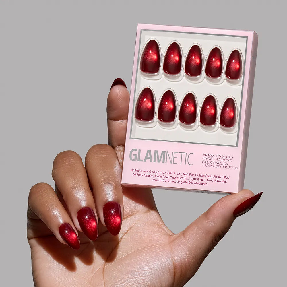A hand with long, oval-shaped red metallic glamnetic press-on nails holds a Frosted Cranberry box against a plain gray background.