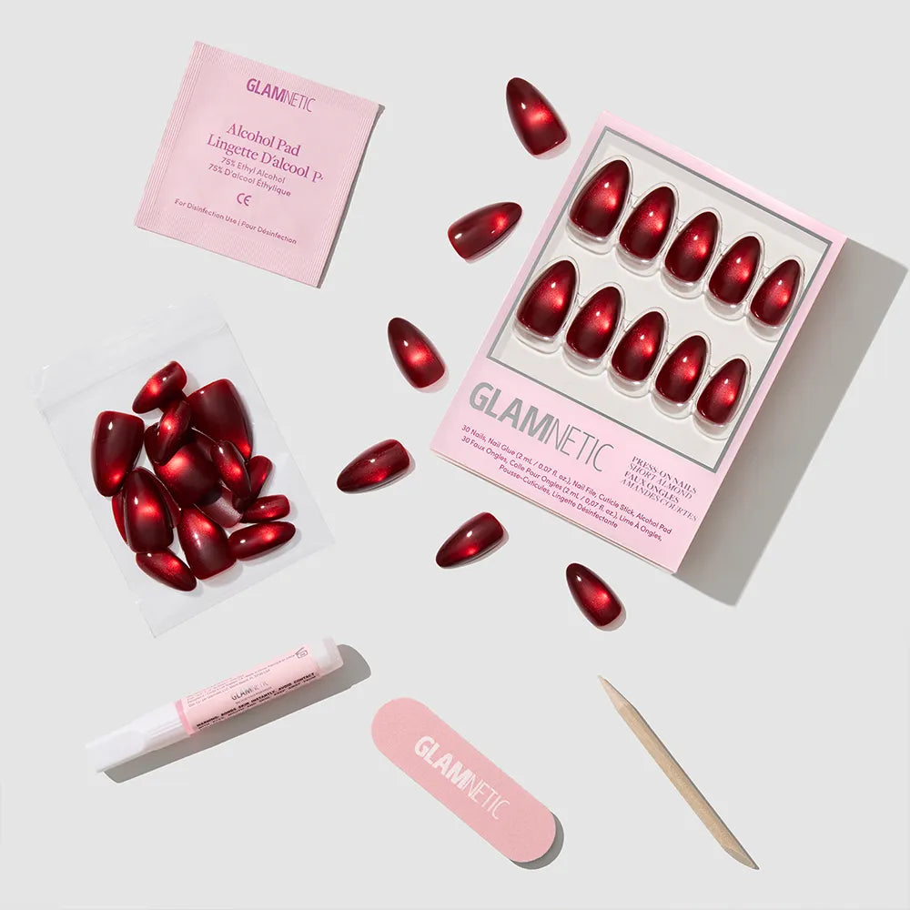 The glamnetic Frosted Cranberry set includes red short almond nails, a pink nail file, cuticle stick, glue tube, alcohol pad, and extra nails—perfectly arranged for a festive manicure.