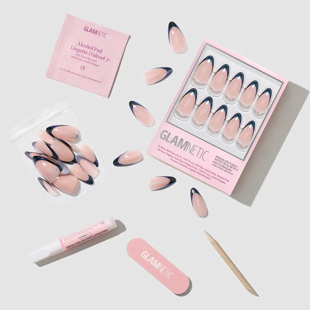 Black Truffle by glamnetic: almond-shaped pink and navy blue press-on nails with French tips, plus alcohol pad, glue tube, nail file, cuticle stick, and extra nails—all arranged neatly on a light gray background.