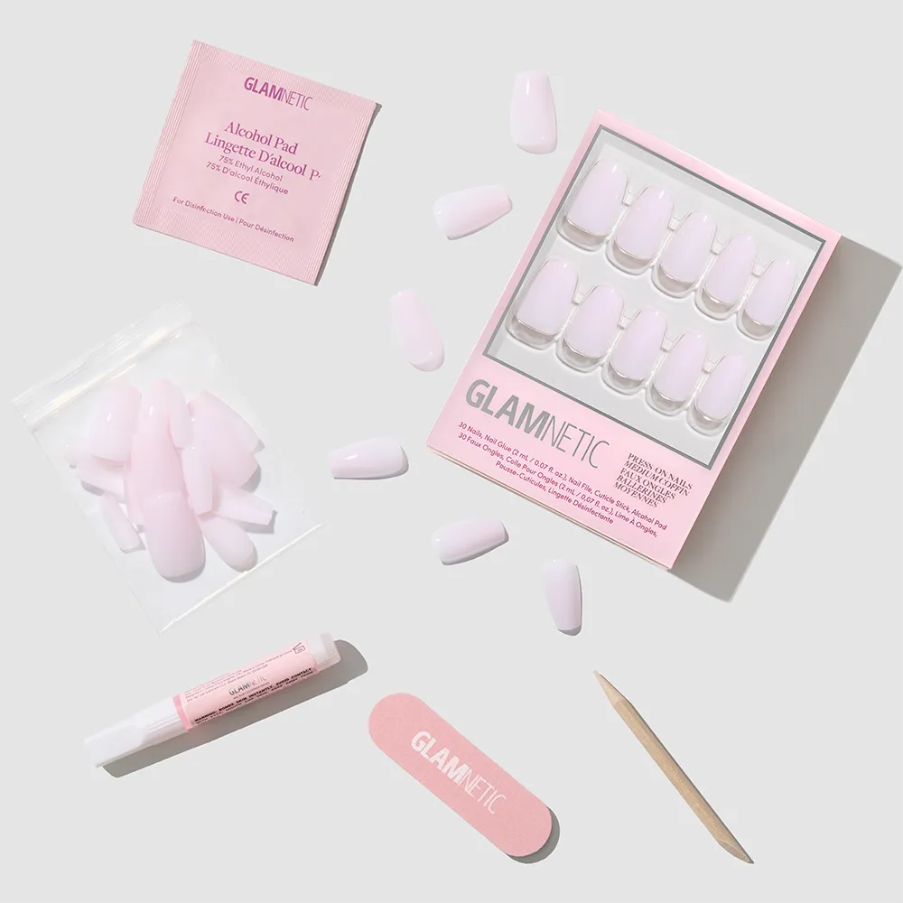A glamnetic Blush Dream press-on nails kit features soft pink medium coffin nails, a nail file, cuticle stick, nail glue, alcohol pad, and extra nails arranged on a light gray background.