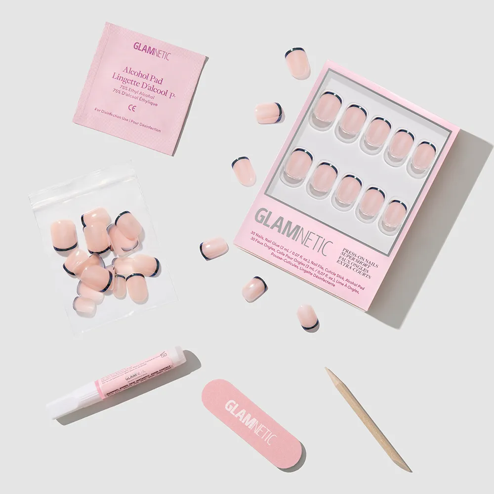 Flat lay of the glamnetic Burnt Miso Press-On Nails kit, showing pink and black French tips with a glossy finish, plus glue tube, nail file, cuticle stick, alcohol pad, and extra nails on a light gray background.