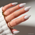 A hand with long, almond-shaped nails painted in glamnetic's Clouded—a glossy, pale lavender polish—paired with a white sweater and two gold rings.