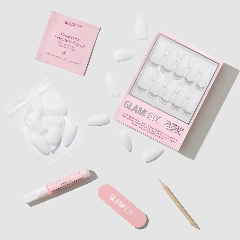Clouded by glamnetic: elegant, almond-shaped milky mani press-on nails with extra nails, alcohol pad, nail glue, file, and cuticle stick—neatly arranged on a light gray background. Packaging features "glamnetic" in pink.