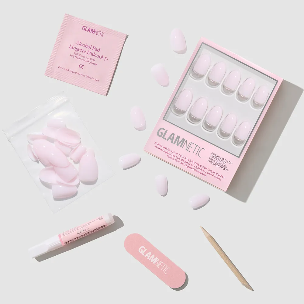 A flat lay of glamnetic's Doll Cheeks press-on nail kit, featuring short oval nails, extra loose nails, a nail file, cuticle stick, alcohol pad, and nail glue—everything for a salon-quality manicure on a light gray background.