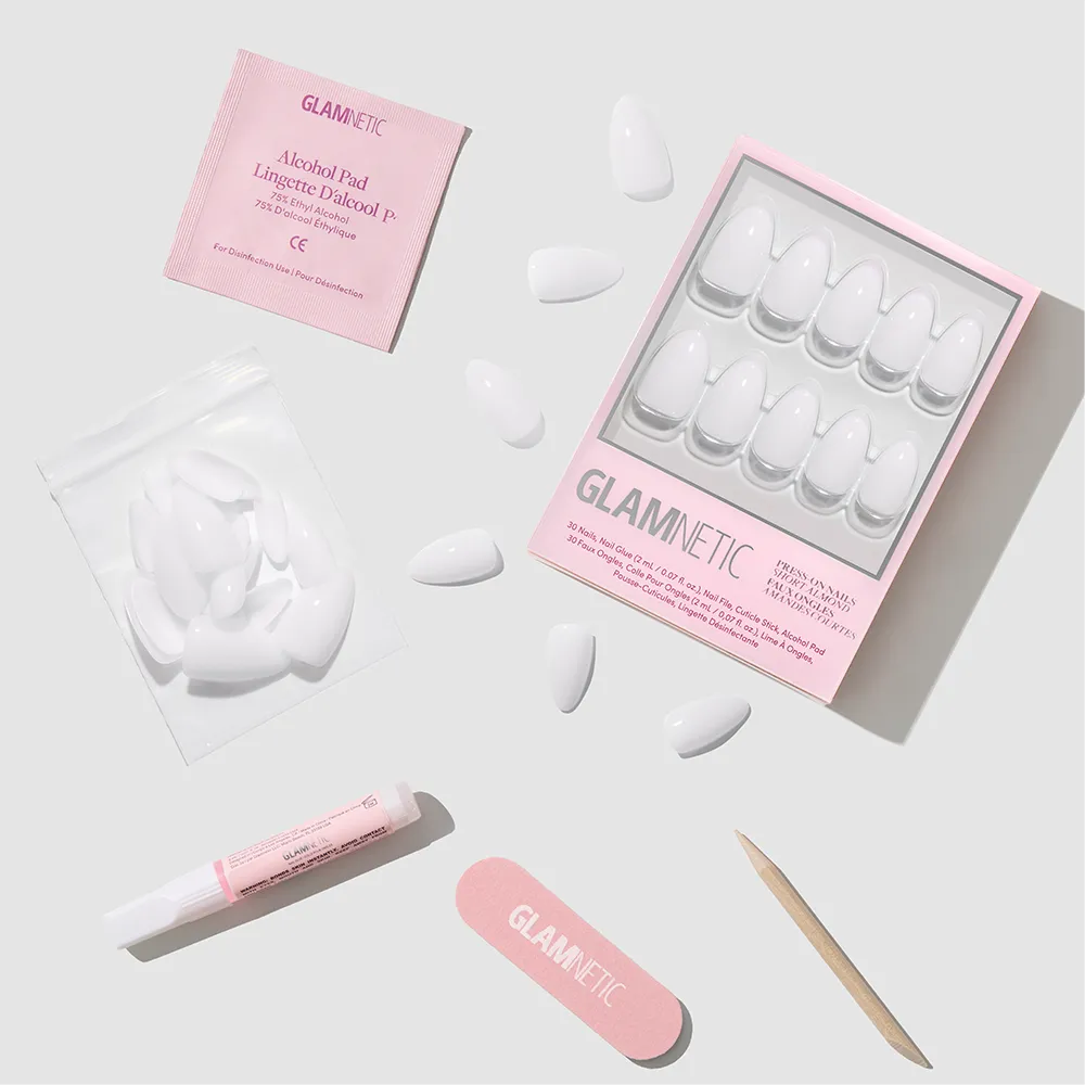 A flat lay of the glamnetic Milky White press-on nail kit includes short almond-shaped nails, a pink nail file, wooden cuticle stick, glue tube, alcohol pad, and extra nails for an easy salon-quality manicure at home.