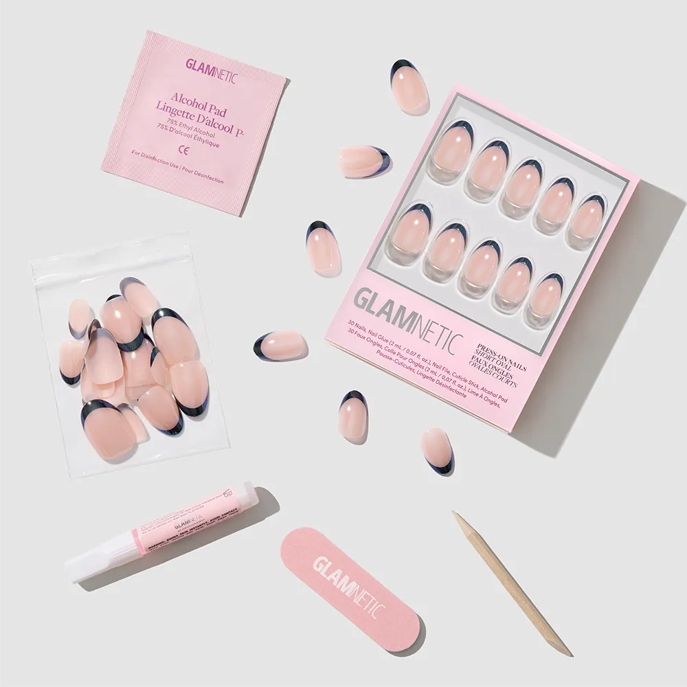The Glamnetic Smoke Salt French tip press-on nails feature a glossy glazed finish in a short oval shape, and come with an alcohol pad, nail glue, nail file, wooden cuticle stick, and extra nails arranged on a light surface.
