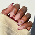 A hand wears glamnetic's Arizona State Sun Devils Press-On Nail Set, showing almond-shaped, salon-quality nude nails with maroon French tips and a gold fork symbol on the ring finger, paired with a light beige sleeve.