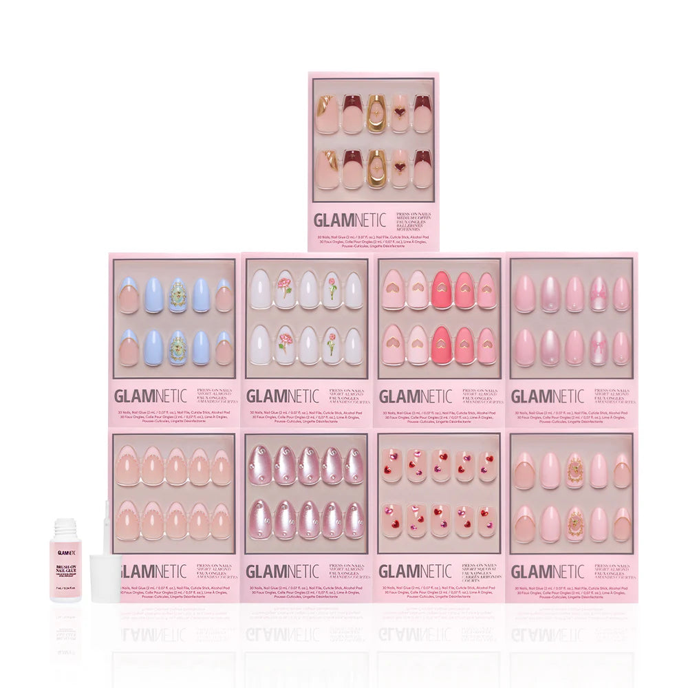 Ten boxes of glamnetic Love in 3D press-on nails are stacked pyramid-style, displaying pastel pink designs with almond shapes and 3D pearl accents. A small bottle of nail glue is placed at the front left.