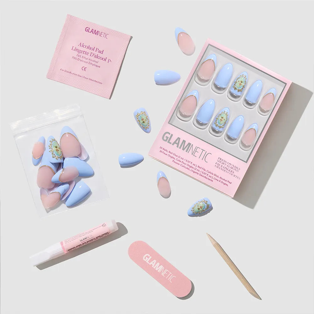 A flat lay of glamnetic's Angel in Blue press-on nails kit, featuring blue and pink short almond nails, nail glue, cuticle stick, pink file, alcohol pad, and extra nails—all neatly arranged on a light background.