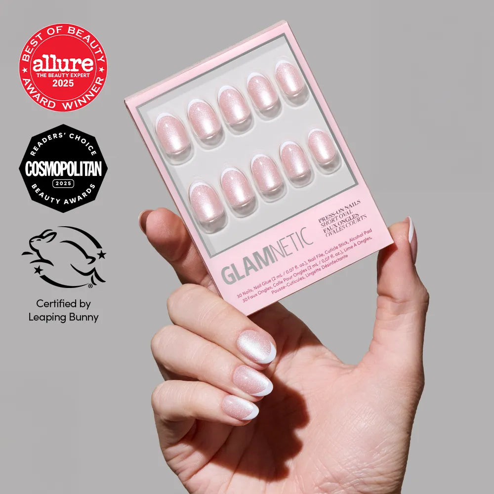 A hand with iridescent white French tip Angelic Touch press-ons by glamnetic holds the box. To the left, award badges from Allure, Cosmopolitan, and Leaping Bunny are displayed.