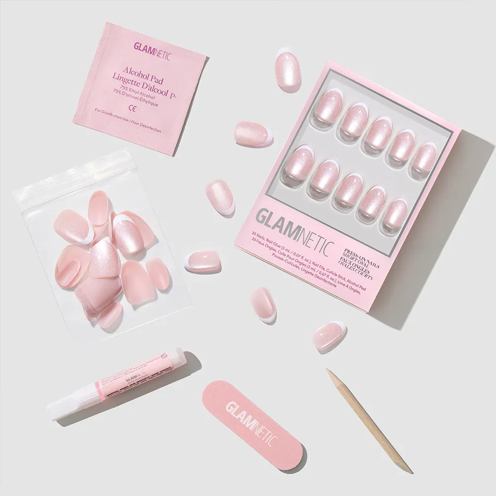 A set of Angelic Touch pink press-on nails by glamnetic in a short oval style, with nail file, cuticle stick, adhesive tube, alcohol pad, and extra nails arranged neatly on a white surface. All accessories feature the glamnetic brand.