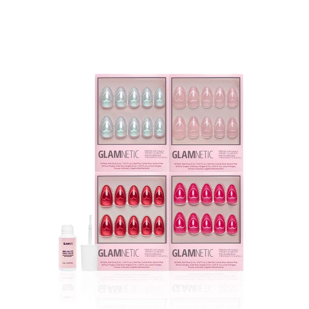 Four boxes of glamnetic Cupid's Magnetic Hearts press-on nails in pastel blue, coral, pink, and red are arranged in two rows. To the left is a small bottle of glamnetic nail glue with applicator. All set against a white background.