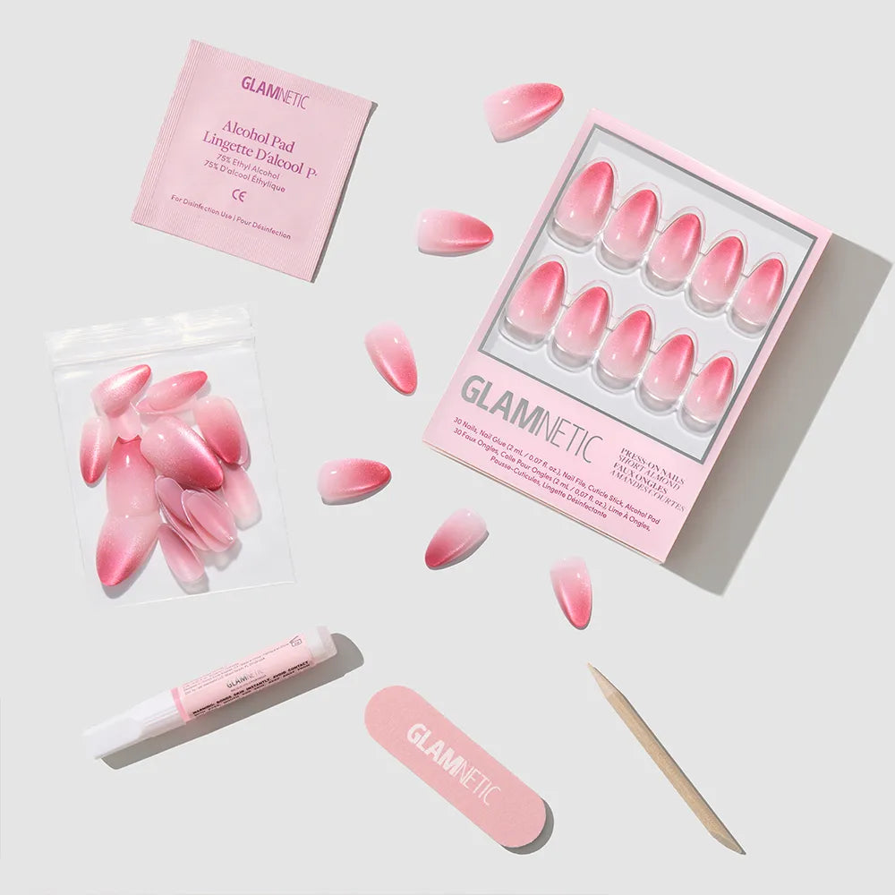 The glamnetic Faded Feelings set includes pink velvet ombré almond press-on nails, a nail file, wooden cuticle stick, alcohol pad, glue tube, and extra nails arranged neatly on a light gray background.