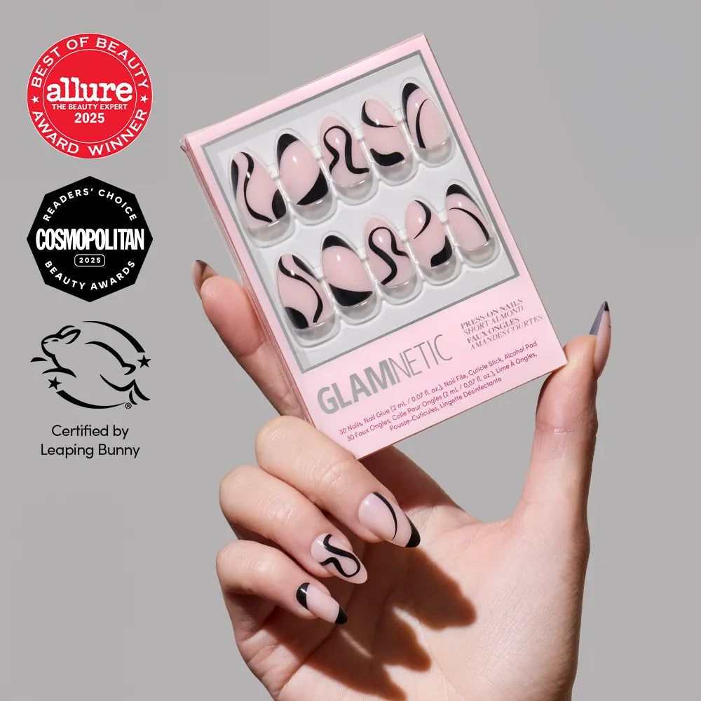 A hand with a pink and black minimalist design on short almond nails holds a box of glamnetic Ink Wave glossy press-on nails featuring the same look. Award and certification logos appear on the left side of the image.