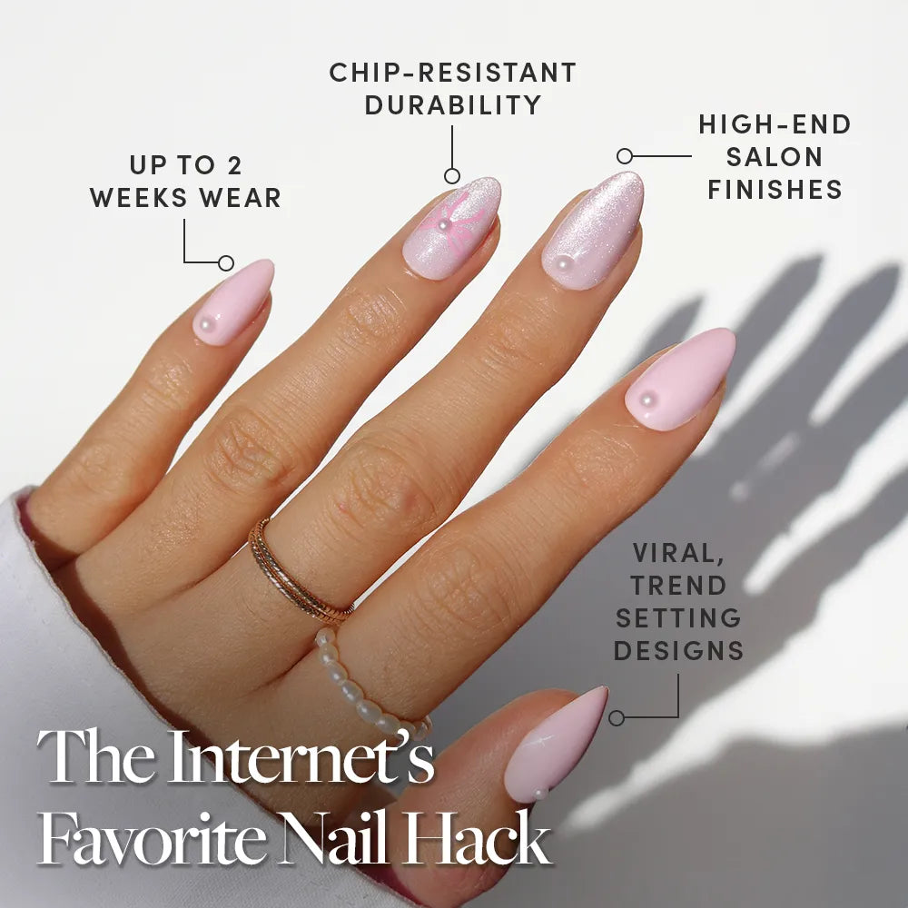 A hand with long, almond-shaped Love Knot press on nails by glamnetic features 3D pearl accents and a shimmery finish. Benefits: 2 weeks wear, chip-resistant, high-end, trend-setting design. Rings and natural sunlight complete the look.