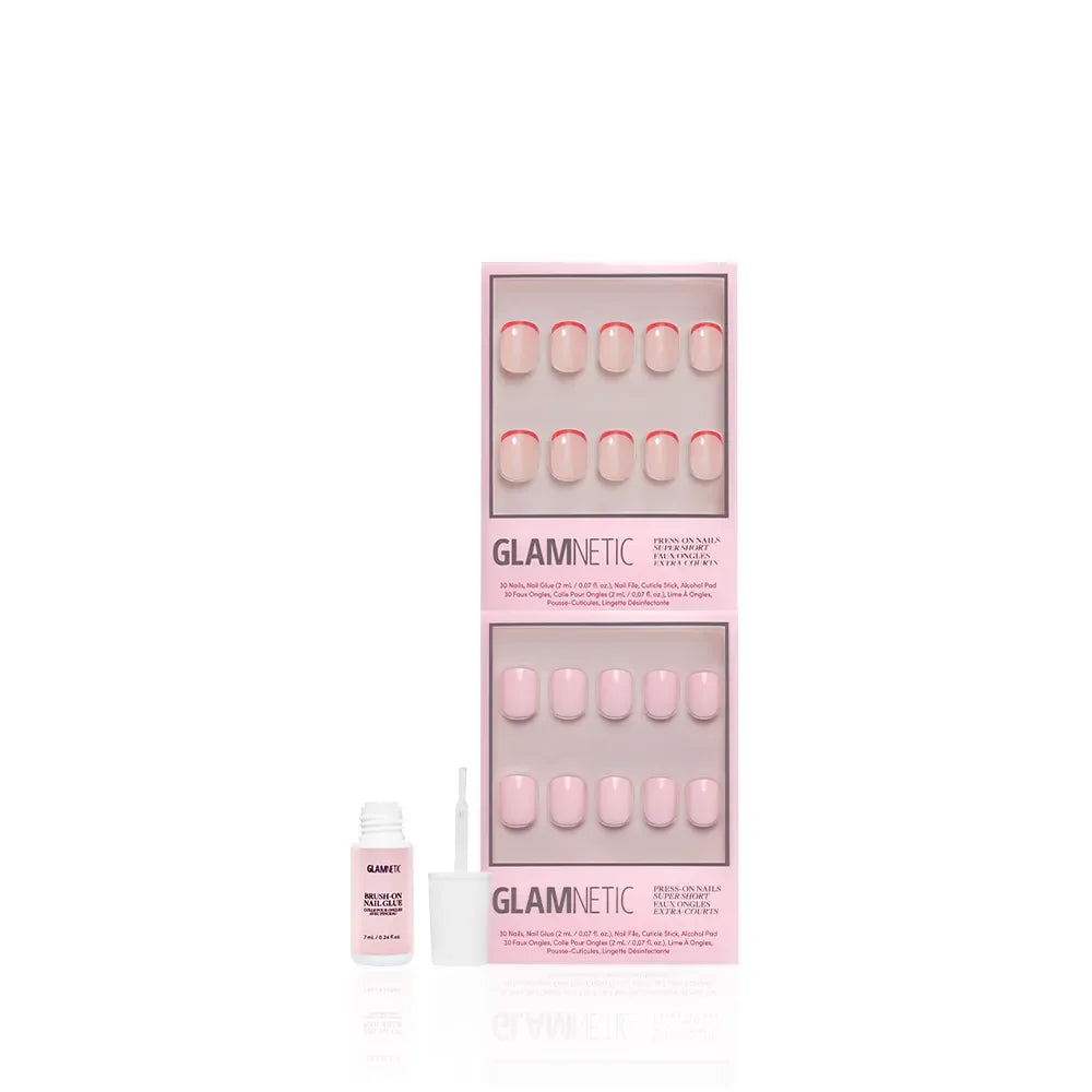 A box of glamnetic Super Short & Sweet press-on nails in light pink with subtle French tips, displayed with two trays of nails and an open nail glue bottle with a brush.