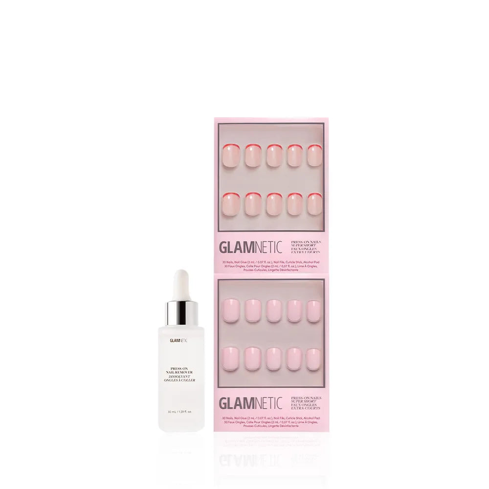 A super short Glamnetic Super Short & Sweet press-on nail set in light pink shades with red-accented French tips, displayed in two pink boxes beside a white Glamnetic Nail Adhesive bottle.