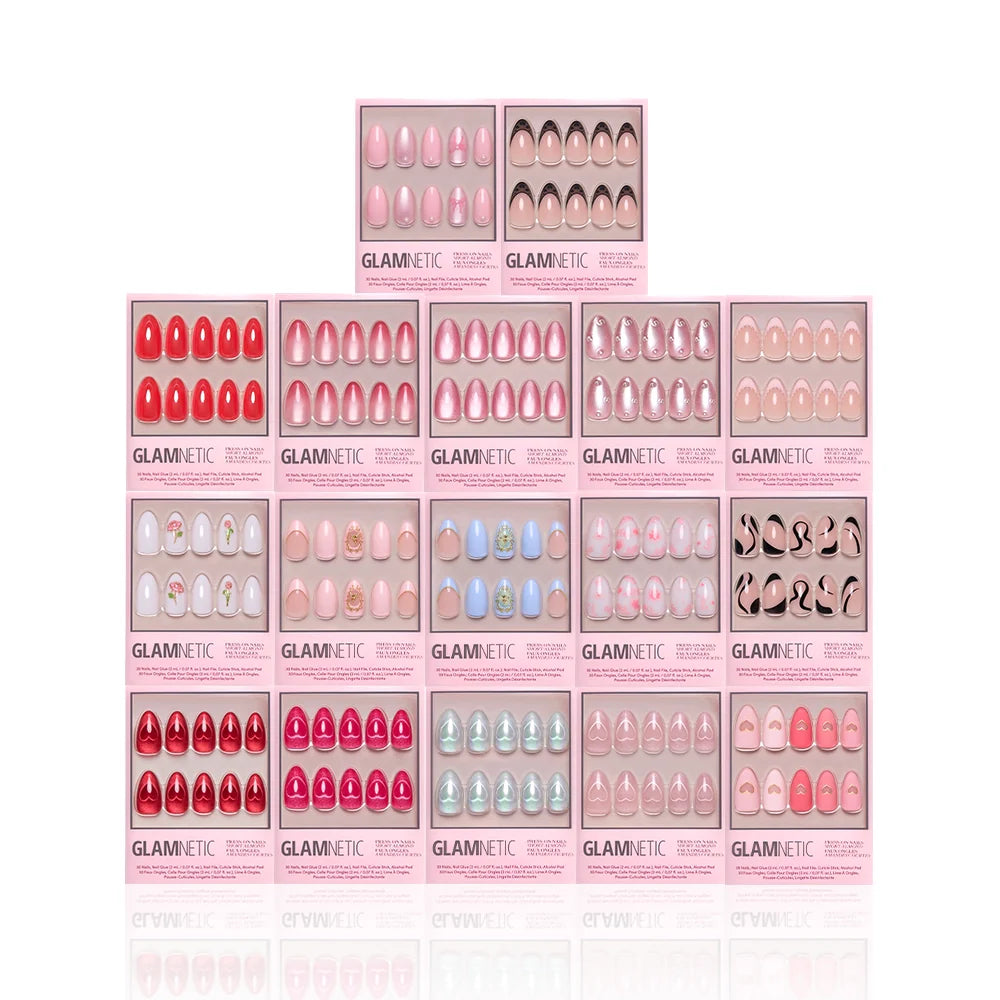 Several Glamnetic The Almond Crush press-on nail sets in pink boxes are stacked in a pyramid, displaying a range of styles like solid, ombré, glitter, 3D nail art, and patterned designs.