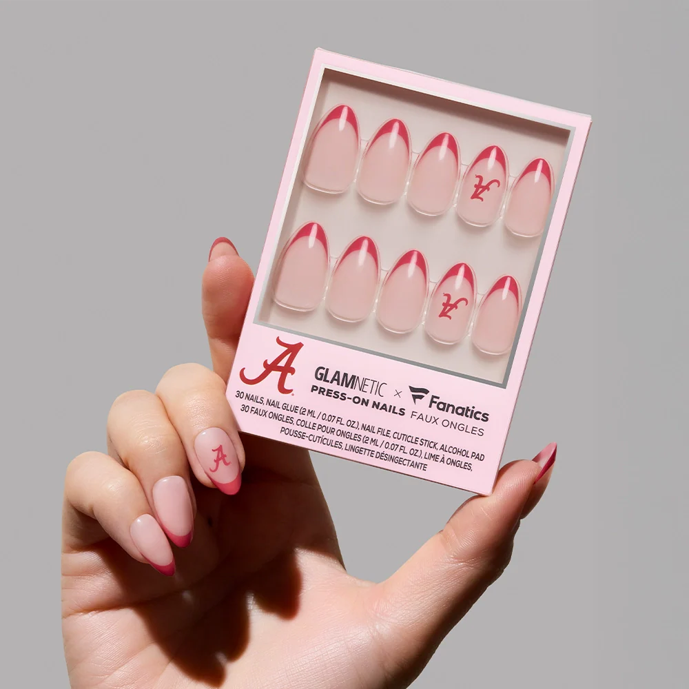A hand holds the Alabama Crimson Tide Press-On Nail Set by glamnetic—pink and clear press-ons with red tips, A team logo, and ram graphic. The packaging features glamnetic and is perfect for showcasing your Alabama pride.