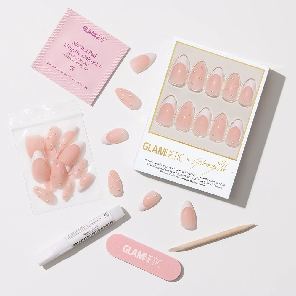 Flat-lay of the full nail kit contents: the boxed nail set, loose nails in a ziplock pouch, a Glamnetic nail glue pen, a pink nail file, a wooden cuticle stick, and an alcohol pad—all arranged neatly against a white background.

