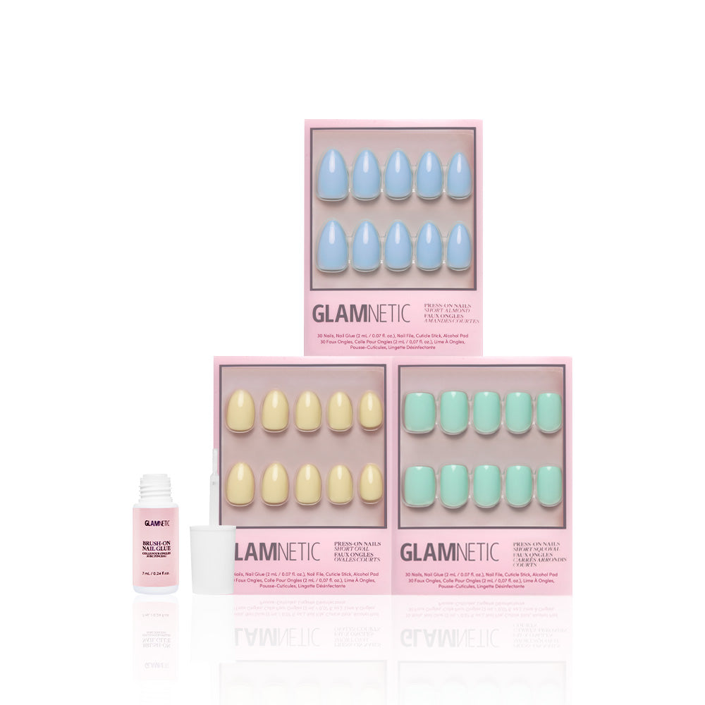 Three boxes of glamnetic’s Anns Palette press-on nails in pastel blue, yellow, and green are displayed—perfect for spring. An open glamnetic nail glue bottle with an applicator is shown to the left on a white background.
