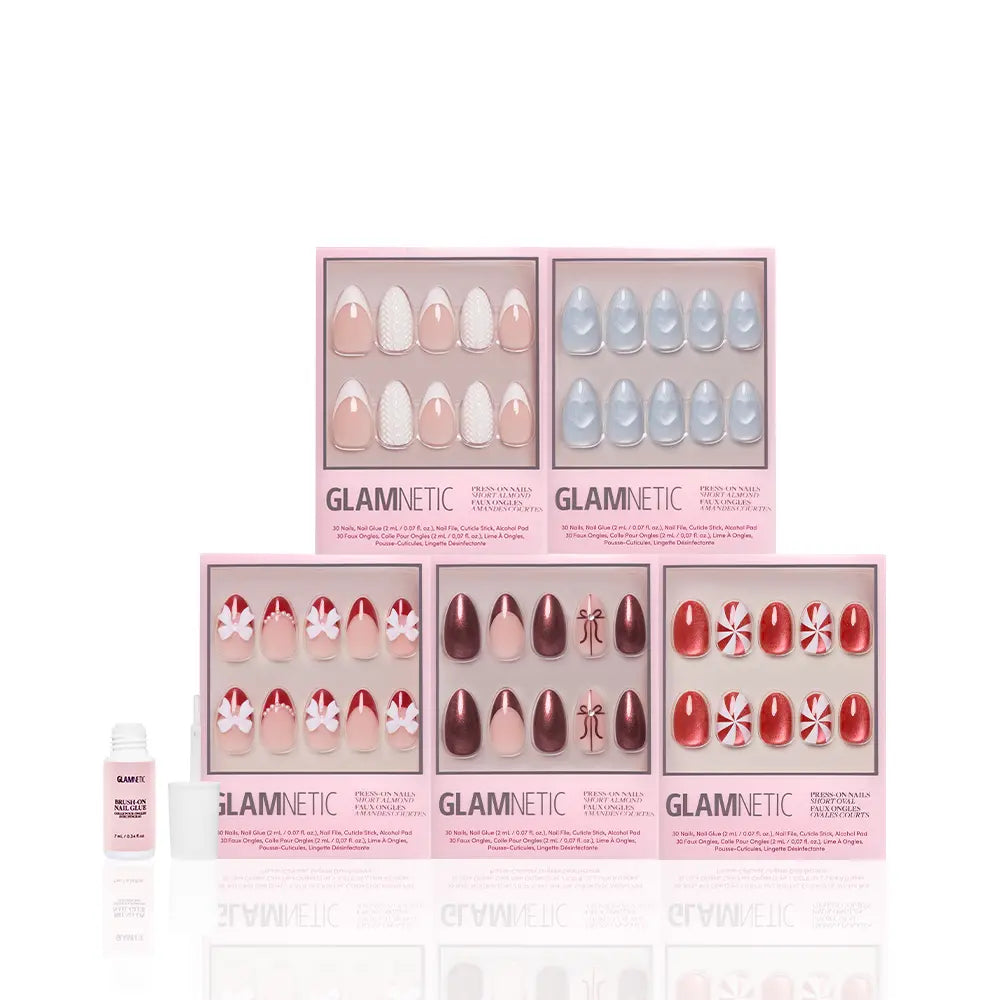 Six boxes of glamnetic Ann's Festive Five almond press-on nails in pink, red, blue, white, and peppermint patterns are displayed in two rows, with a glue bottle in front—ideal for party-ready manicures or a festive holiday nail look.