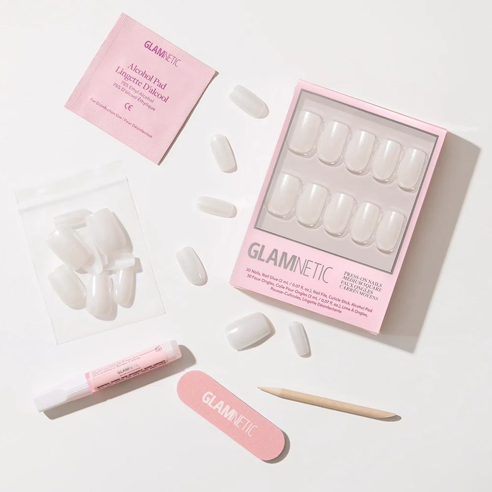 The Bailey vegan nail kit by glamnetic includes medium square semi-transparent nails, a pink nail file, wooden cuticle stick, glue tube, alcohol pad, spare nails in a bag, all in a pink glamnetic box on a white surface.