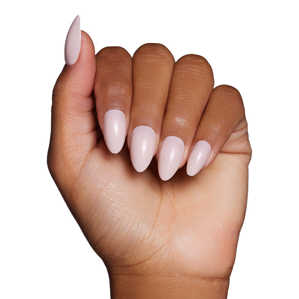 A hand with medium brown skin displays the glamnetic Ballet Pink Nail Set in a short almond shape with a glossy finish against a white background.