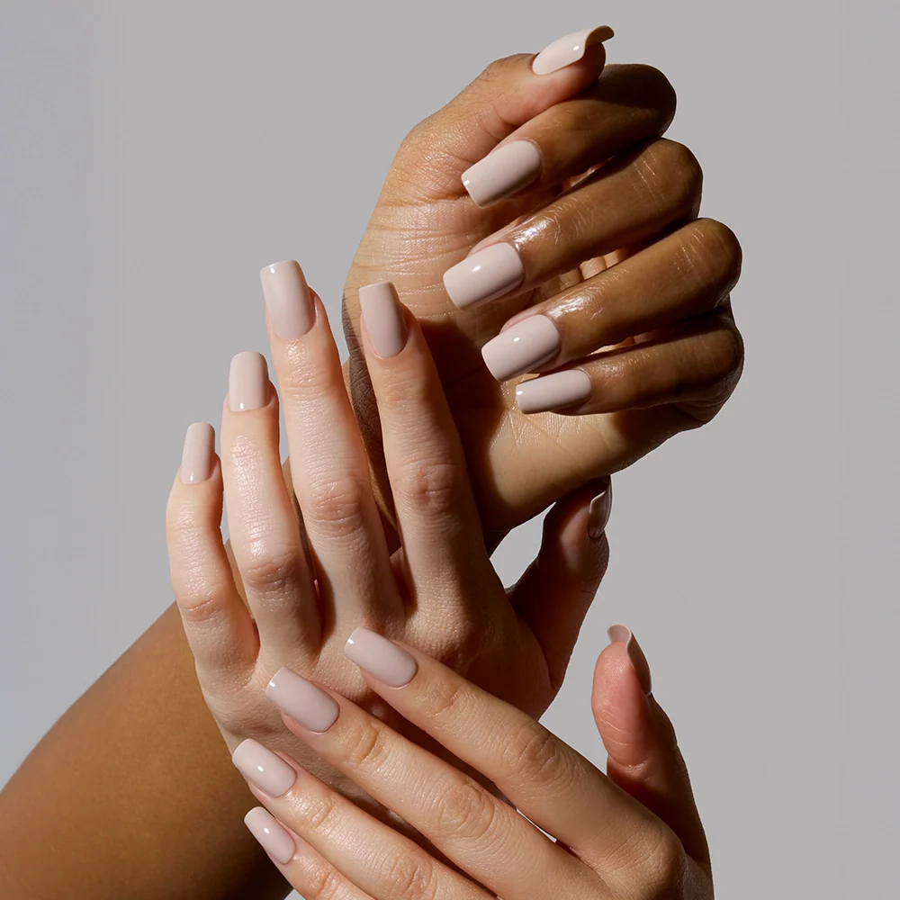 Three hands with varying skin tones showcase glamnetics Bare Bliss nude nail set, each featuring medium square, manicured nails. The subtle elegance of the polish stands out against a plain light gray backdrop.