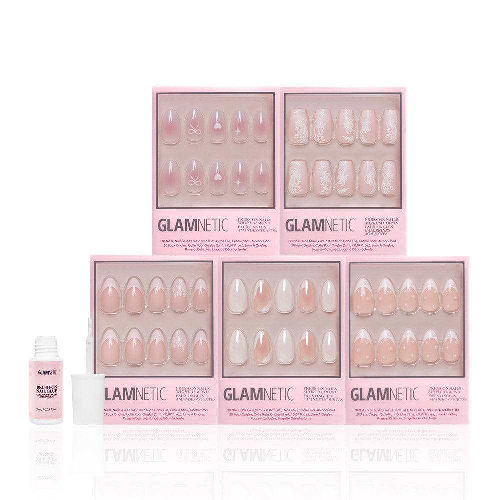 Six sets of glamnetic Be Mine pink and white press-on nails, featuring short almond French tip designs and semi-transparent accents, are displayed in two rows in pink glamnetic boxes. A small bottle of nail glue with an open cap sits on the left.