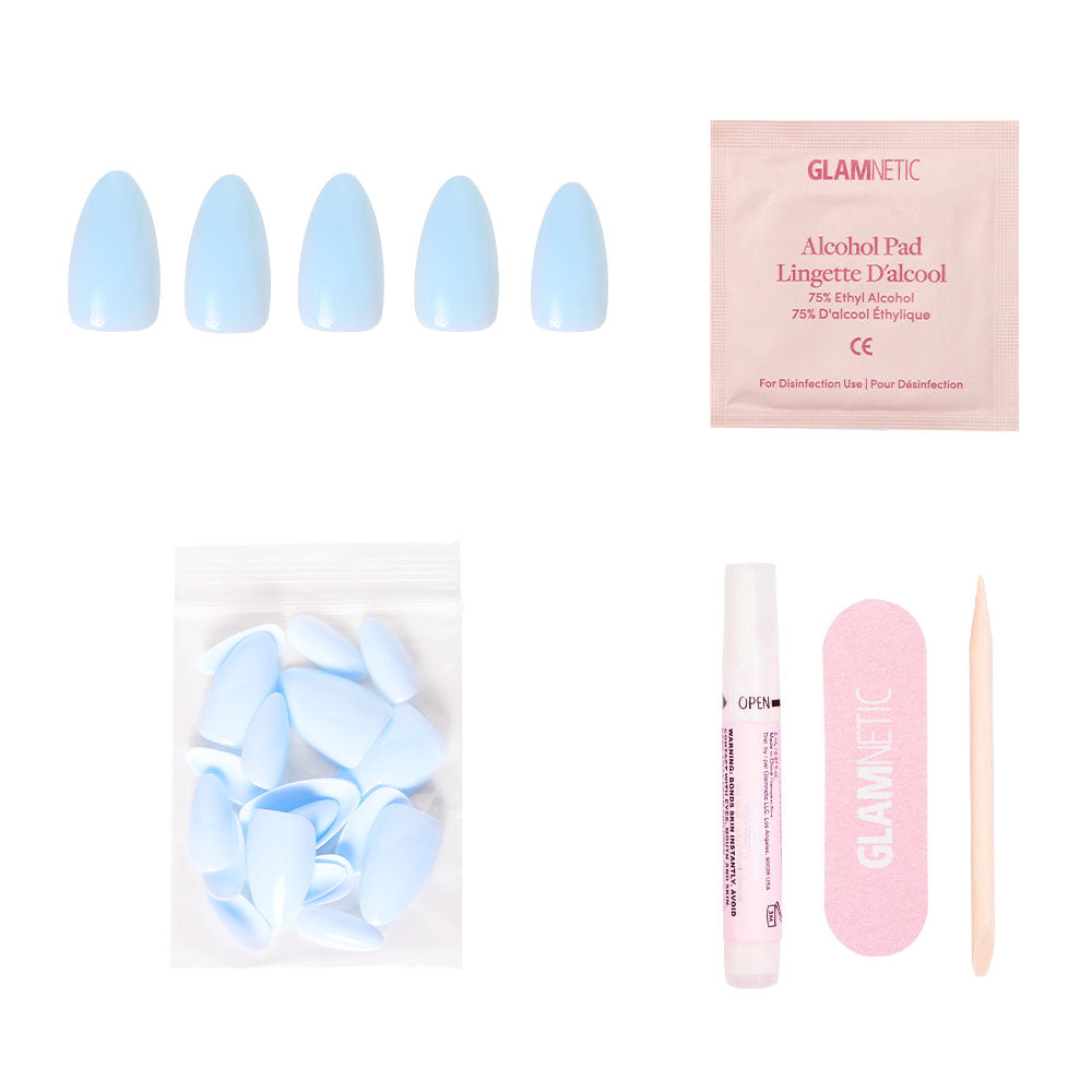 The glamnetic Blueberry Milk set includes glossy blue press-on nails, a nail glue pen, extra nails, an alcohol pad, pink nail file, and wooden cuticle stick—arranged on a white background.