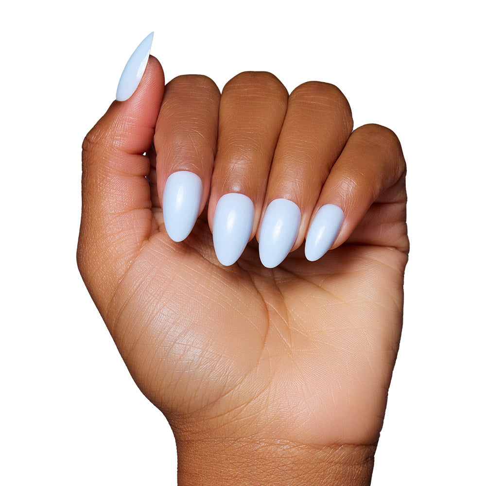 A hand with medium brown skin shows long, almond-shaped nails in a glossy light blue shade, featuring the Blueberry Milk set by glamnetic, against a white background.