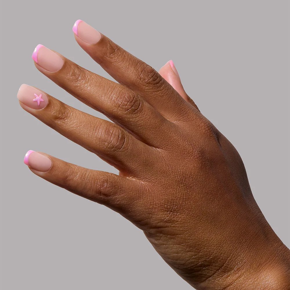 A hand wears glamnetic’s Blush Dunes press-on nails, featuring soft pink chrome tips and a white star accent, shown against a plain gray background.