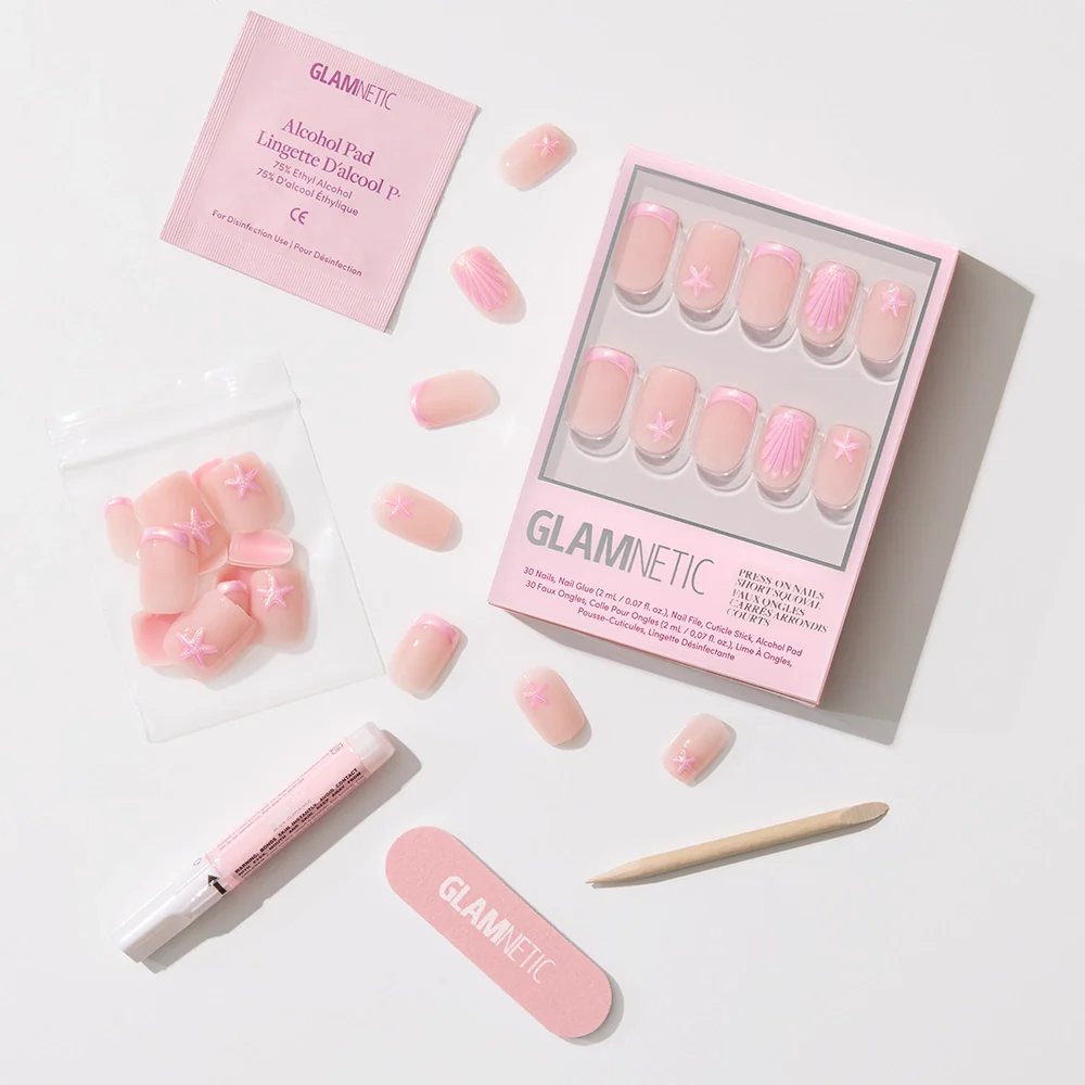 The Blush Dunes press-on nail set by glamnetic features soft pink chrome tips with white star and shell designs, arranged with nail tools on a light background. Packaging displays the glamnetic logo—perfect for tropical getaways.