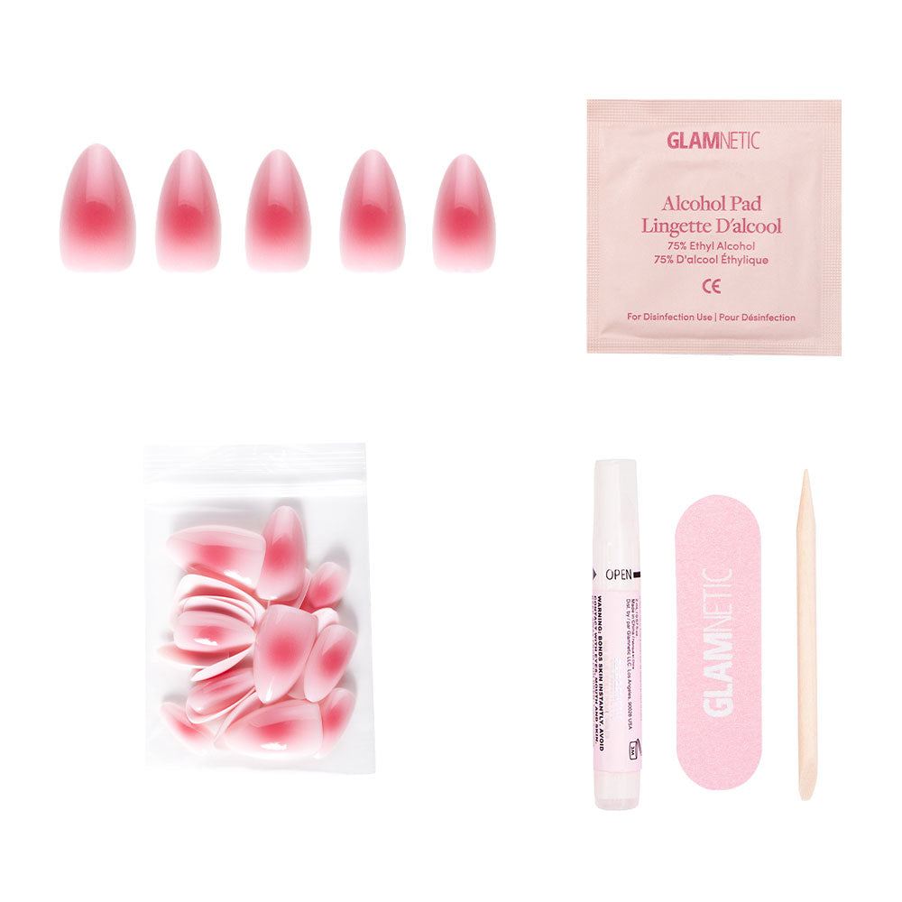 The glamnetic Blushing Aura nail set includes short almond ombre pink nails with an abstract dark pink center, plus extra nails, nail glue, a pink file, alcohol pad, and wooden cuticle stick on a white background.