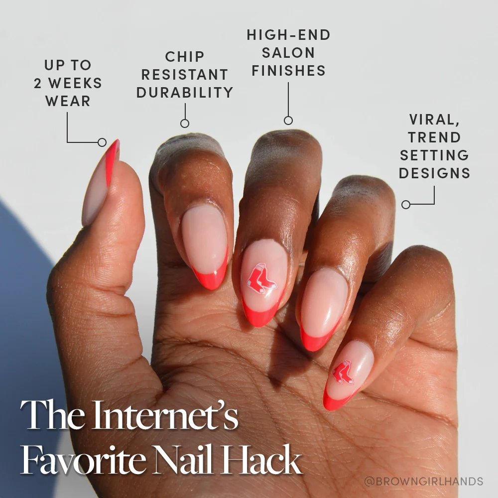 A hand with almond-shaped nails featuring a pink base and bold red tips, some with red designs. Showcasing the glamnetic Boston Red Sox Press-On Nail Set: salon quality, chip-resistant, trendy designs, up to 2 weeks wear.