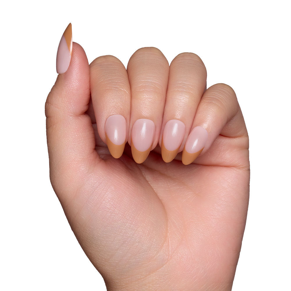 A hand with glamnetic Café Crème almond-shaped, reusable nails—nude base and brown French tips—is displayed against a white background for a cozy vibe.