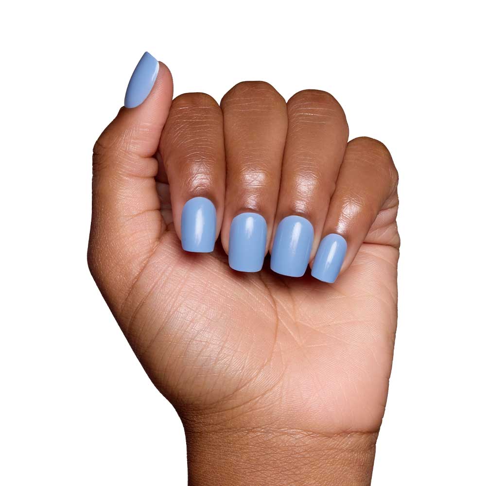 A hand with medium brown skin displays short squoval nails painted in glamnetic’s Cashmere Blue, a glossy light blue shade. The fingers are gently curled inward against a plain white background.